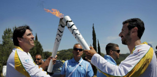 Olympic flame second torch bearer former volleyball player Giovane Gavio from Brazil passes the torch to third bearer Dimitrios Mougios as they attend the Olympic flame lighting ceremony for the Rio 2016 Olympic Games on the site of ancient Olympia